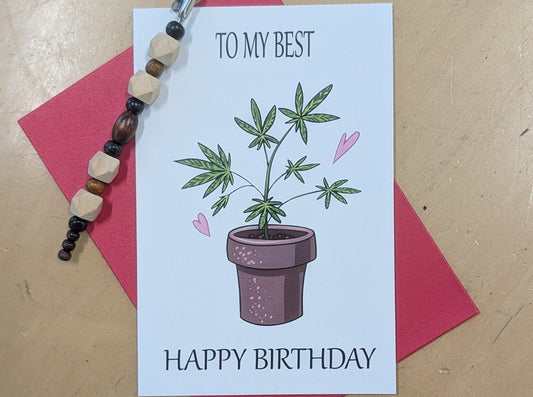 A birthday card with a potting plant illustration and the text 'TO MY BEST FHAPPY BIRTHDAY' lies with a red envelope.